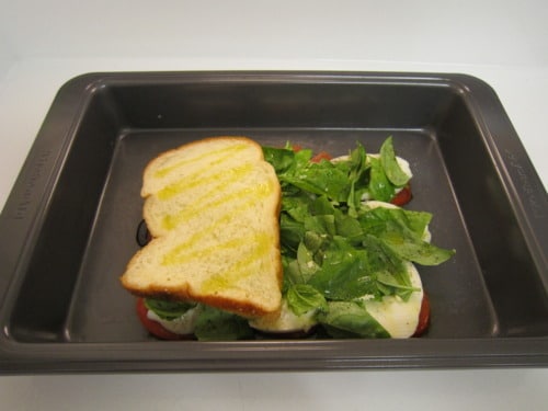 Bread slices layered with fresh basil and mozzarella in a baking pan, ready to be baked.