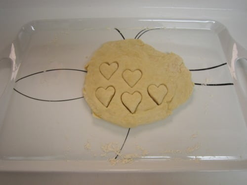 Buttermilk cookie dough rolled out on a tray with heart shapes cut out, ready for baking.
