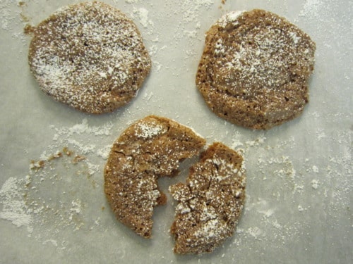 This image shows chocolate macaroons dusted with powdered sugar, with one cookie broken in half to reveal its chewy texture.