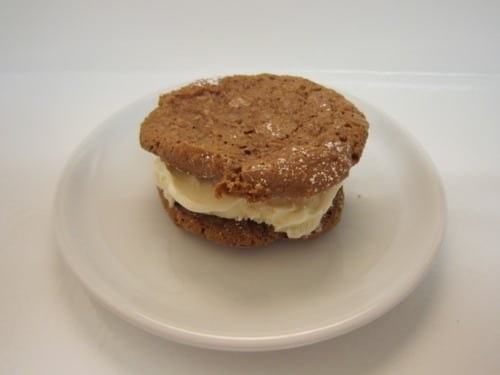 Chocolate macaroon ice cream sandwich on a white plate, filled with a scoop of vanilla ice cream.