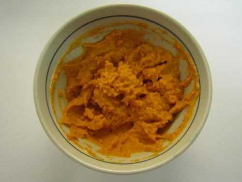Bowl filled with orange-colored mashed mixture or puree on a white surface.