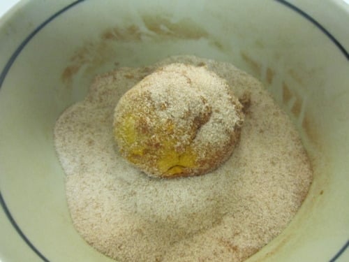 Ball of pumpkin muffin dough being rolled in a bowl of cinnamon sugar coating.