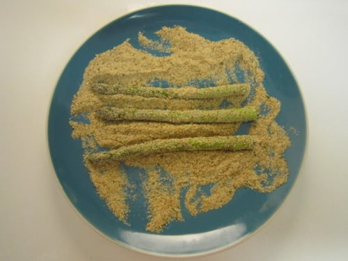 Asparagus spears being coated in panko breadcrumbs on a blue plate for panko-crusted asparagus with soy garlic aioli.