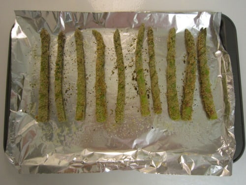 anko-crusted asparagus spears arranged on a foil-lined baking sheet, seasoned and ready for baking.