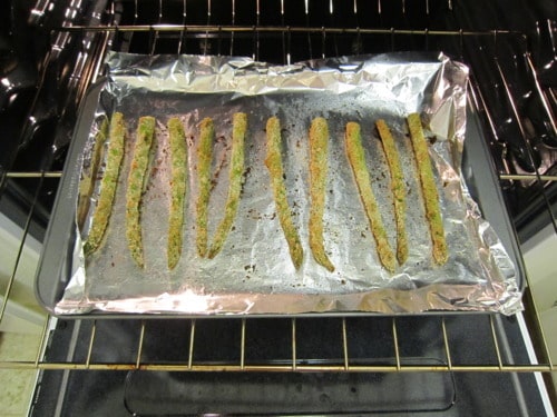 Breaded asparagus spears arranged on a foil-lined baking sheet inside an oven.