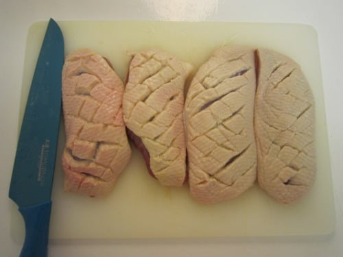 Duck breasts scored with a knife on a cutting board, ready for cooking.