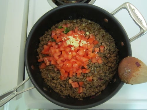 Ground beef cooking in a skillet with diced tomatoes, minced garlic, and chopped jalapeño, prepared for Southwestern sloppy joe sliders.
