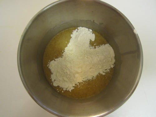 Flour added to a wet mixture in a metal mixing bowl, prepared for strawberry banana orange muffin batter.