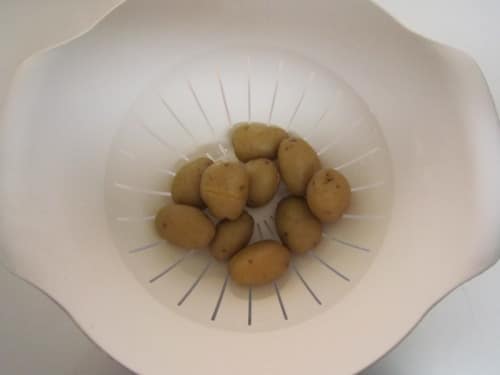 Boiled baby potatoes draining in a white colander for smashed potatoes recipe.