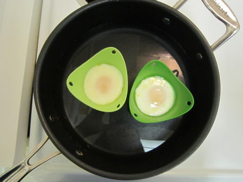 Eggs being poached in green silicone cups placed in a pan of hot water, prepared for serving with asparagus.