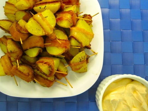 Bacon-wrapped potato bites on toothpicks served with a side of spicy sour cream dip.