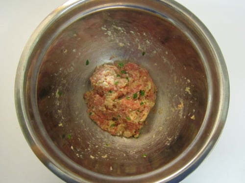 Ground meat mixture with herbs and seasonings in a stainless steel bowl, prepared for meatball parmigiana sliders.
