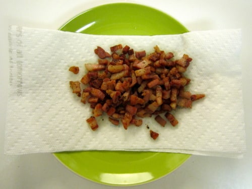 Cooked pancetta pieces drained on a paper towel-lined green plate, prepared for potato salad with pancetta and avocado.