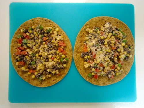 Whole wheat tortillas topped with a mixture of black beans, corn, diced bell peppers, green onions, and goat cheese, prepared for black bean and goat cheese quesadillas.