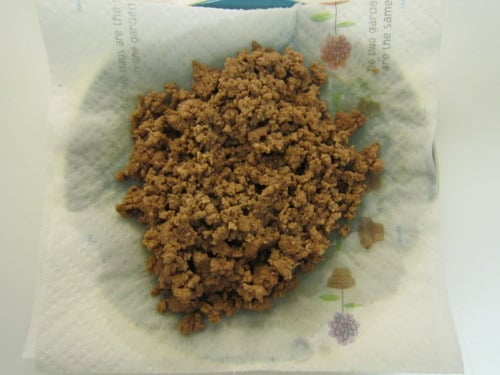Cooked ground beef drained on a paper towel-lined plate, prepared for quick and spicy chili.