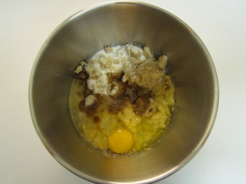 Mixing bowl with mashed banana, egg, brown sugar, white sugar, and vanilla extract for chocolate white chocolate chip banana muffins.