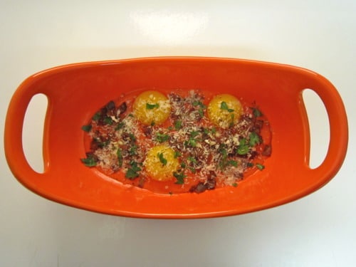 Baked eggs with tomatoes, herbs, and grated cheese in an orange baking dish.
