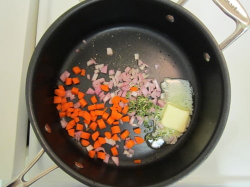 Diced carrots, shallots, fresh thyme, and butter sautéing in a saucepan for turkey and pancetta pot pies.