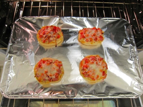 English-Muffin Breakfast Pizza baking on a foil-lined tray in an oven.