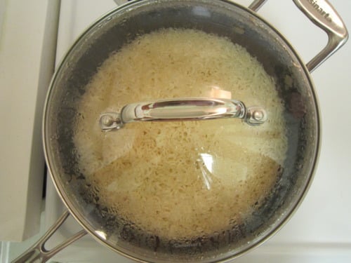 Pot of white rice cooking with a glass lid on a stovetop.