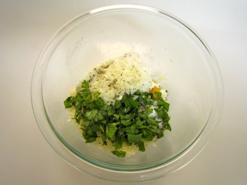 Ricotta cheese, chopped fresh basil, shredded mozzarella, and seasonings in a glass bowl, prepared for stuffed shells with arrabbiata sauce.