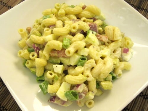 Macaroni salad with pancetta, avocado, red onion, green onion, and chopped egg, served on a white plate.