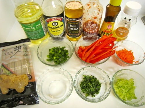 Ingredients for buckwheat noodle salad, including vegetables, sauces, fresh herbs, and seasonings, arranged on a countertop.