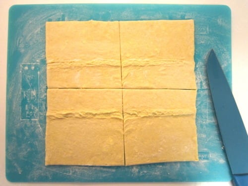 Rolled out pastry dough cut into six rectangles on a floured cutting board with a blue knife, prepared for homemade strawberry Nutella pop tarts.