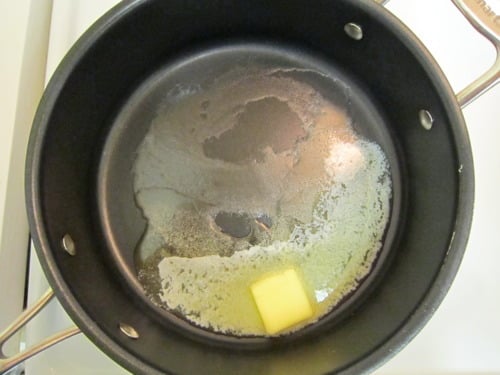Butter melting in a black saucepan, prepared as the base for shrimp, lemon, and herb macaroni and cheese.