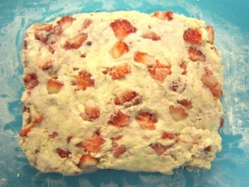 Strawberry scone dough with fresh strawberries on a floured surface, ready to be shaped.