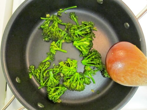 Broccolini being sautéed in a black skillet with a wooden spoon, prepared for Chinese beef with broccoli.