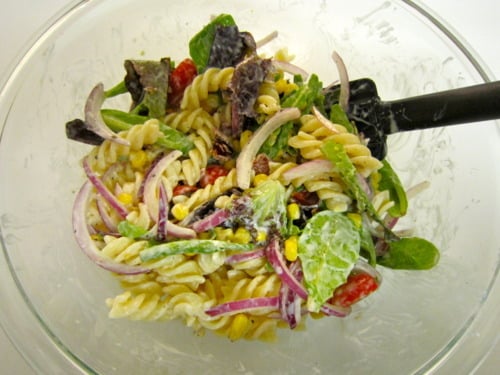 Mixed corn and pasta salad in a glass bowl with rotini, red onion, lettuce, grape tomatoes, and corn, tossed in homemade ranch dressing.