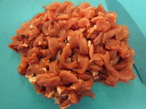 Sliced raw pork on a blue cutting board, prepared for Korean-style pork wraps with chili sauce.