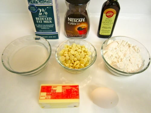 Ingredients for white chocolate chip cappuccino muffins, including milk, instant coffee, vanilla, flour, white chocolate chips, sugar, butter, and an egg.