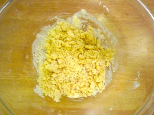 Glass bowl with a crumbly flour and egg mixture prepared for coating orange chicken.