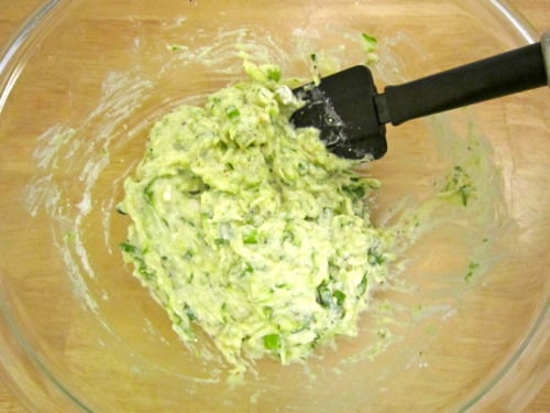 Zucchini and ricotta fritter batter mixed in a glass bowl with a spatula.