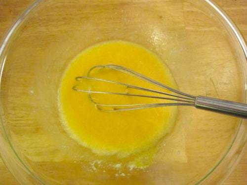 Wet ingredients including mashed banana and melted butter being whisked in a glass bowl, prepared for banana coconut pineapple muffins.
