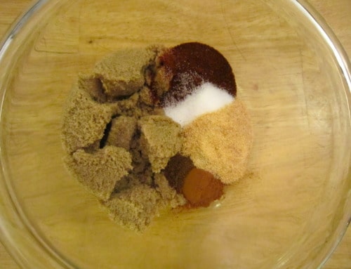 Assorted dry spices and brown sugar measured in a glass bowl, prepared for a sweet and smoky oven spareribs rub.