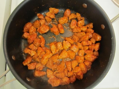 Diced seasoned meat cooking in a black frying pan on a stovetop
