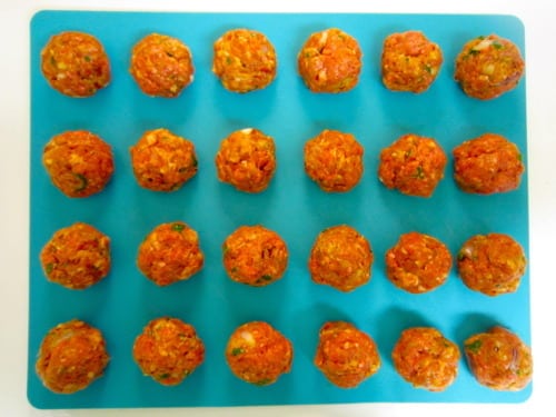 Uncooked meatballs arranged in rows on a blue cutting board, prepared for pizzaiola-style meatballs.