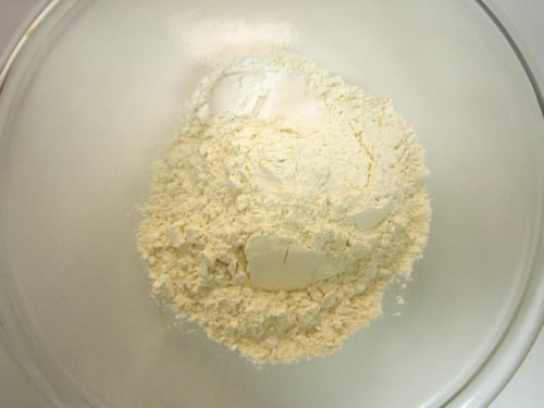 Flour and baking ingredients in a clear mixing bowl, prepared for banana brickle muffin batter.