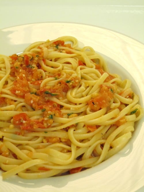 Linguini pasta served with a chunky tomato almond pesto sauce on a white plate.