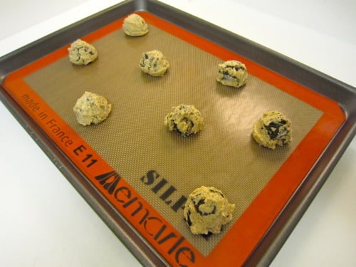 Scoops of cookies and cream cookie dough arranged on a Silpat-lined baking sheet, ready to be baked.