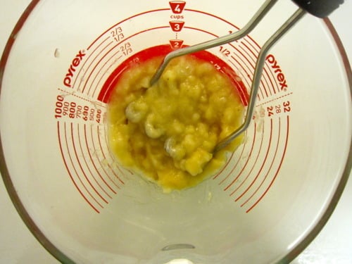 Mashed bananas in a glass measuring cup with a masher, for banana pecan muffins.