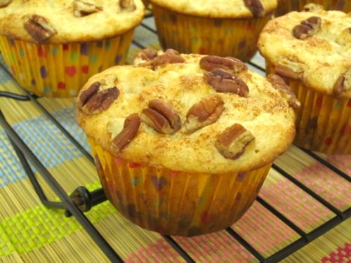 Golden banana muffins topped with chopped pecans cooling on a black wire rack in yellow patterned muffin liners.