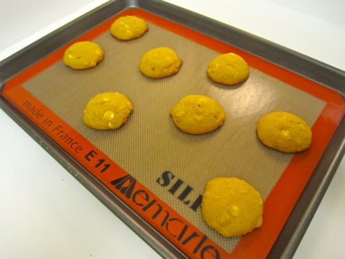 Freshly baked pumpkin white chocolate chip macadamia nut cookies on a Silpat-lined baking sheet.