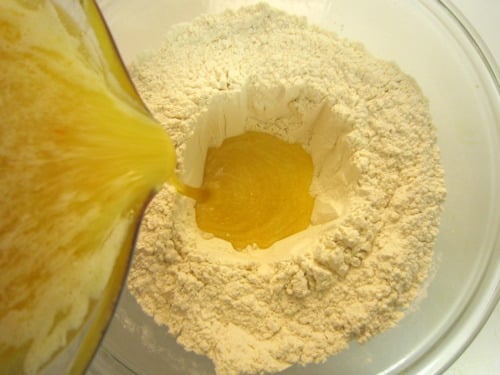 Wet ingredients being poured into a well of dry ingredients in a mixing bowl for orange marmalade muffins.