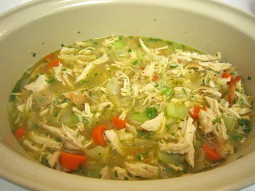 Classic chicken and rice soup in a large pot, filled with shredded chicken, carrots, celery, onions, and herbs in a clear broth.