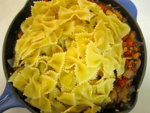 Bowtie pasta layered over sautéed vegetables in a skillet for skillet lasagna.
