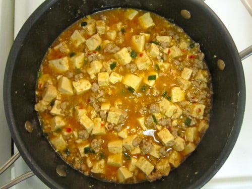 Mapo tofu simmering in a skillet with ground meat, tofu cubes, green onions, and spicy sauce.